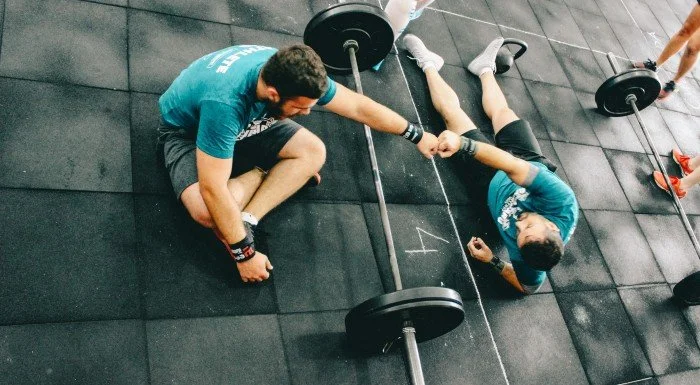 Two friends training together in a gym with a barbell