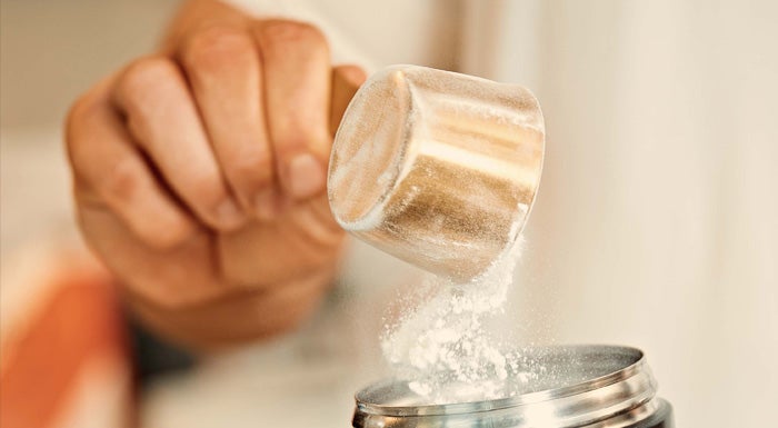 A scoop of creatine being poured into a shaker.